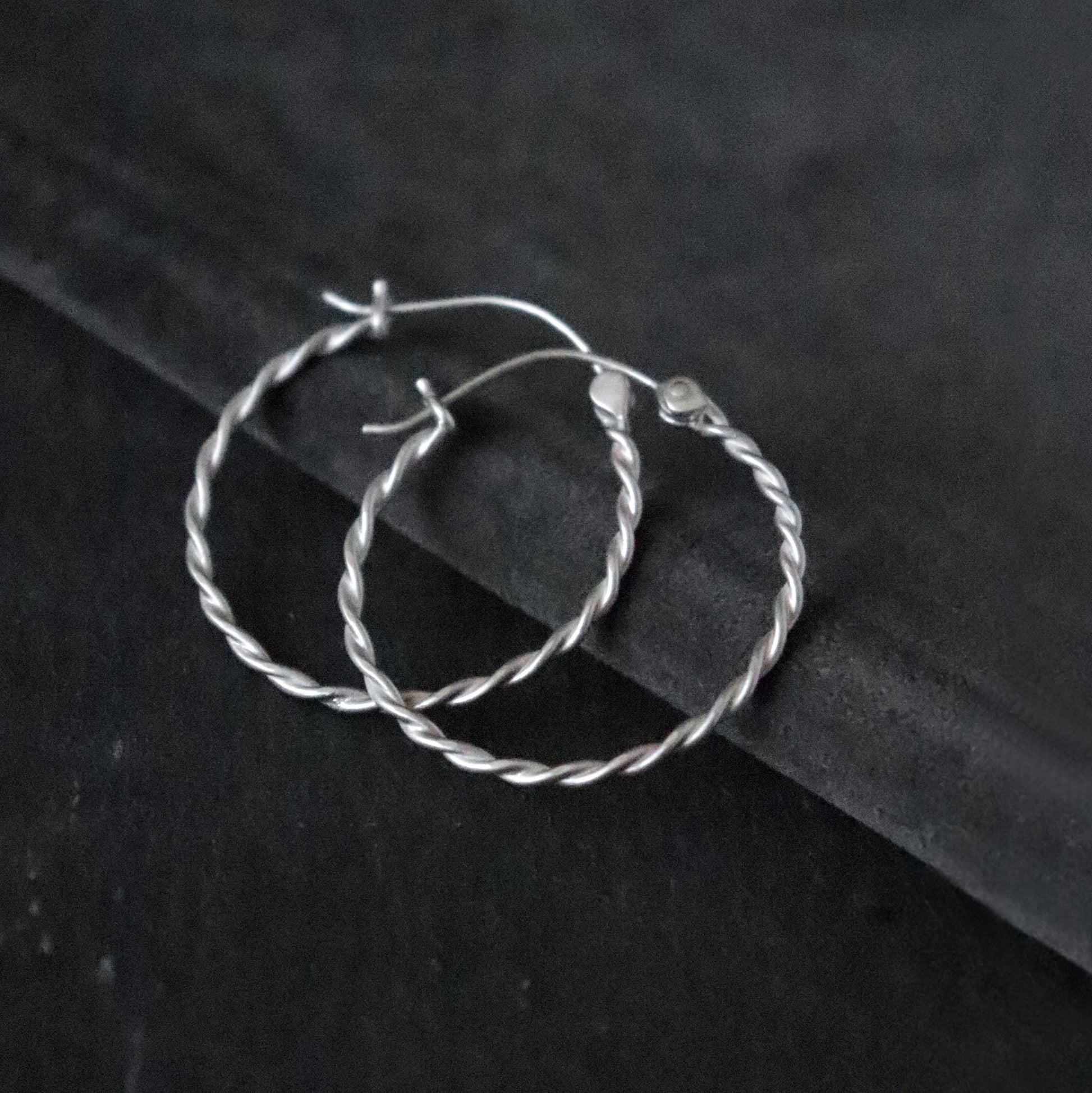 Twisted Silver hoop earrings on a dark grey surface