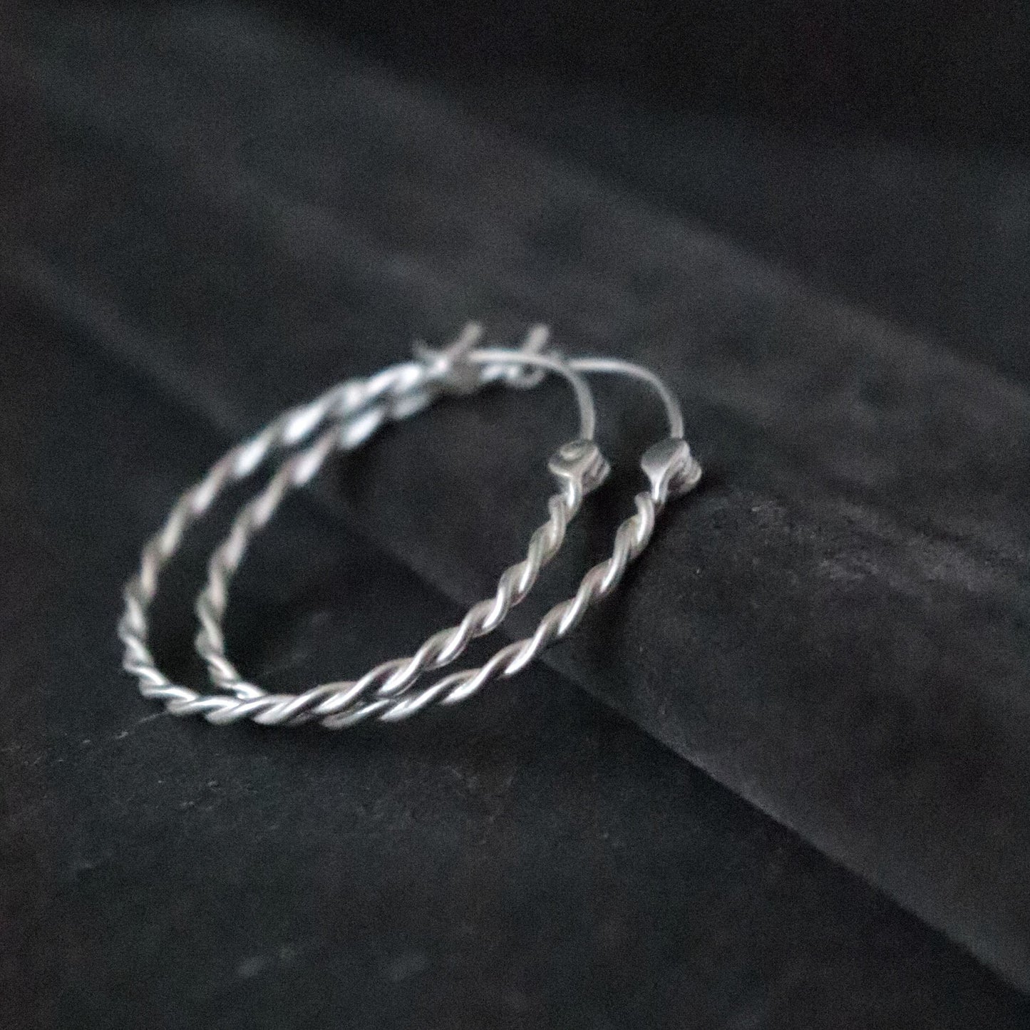 Pair of twisted silver hoop earrings on a dark grey surface