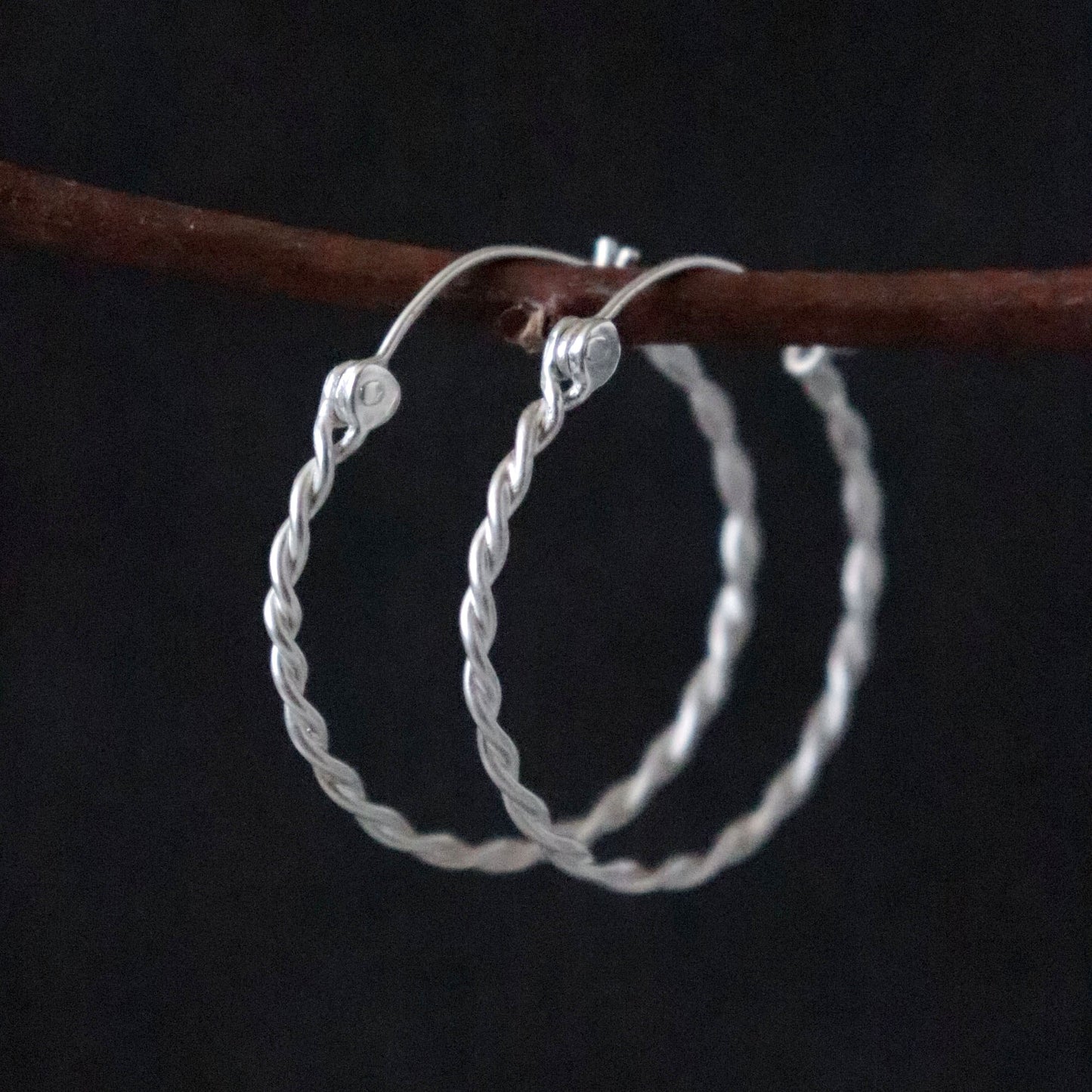 Twisted Silver hoop earrings on a dark background