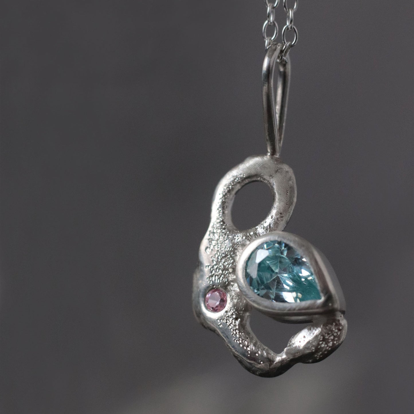 Silver pendant with blue gemstone and pink stone on a dark background