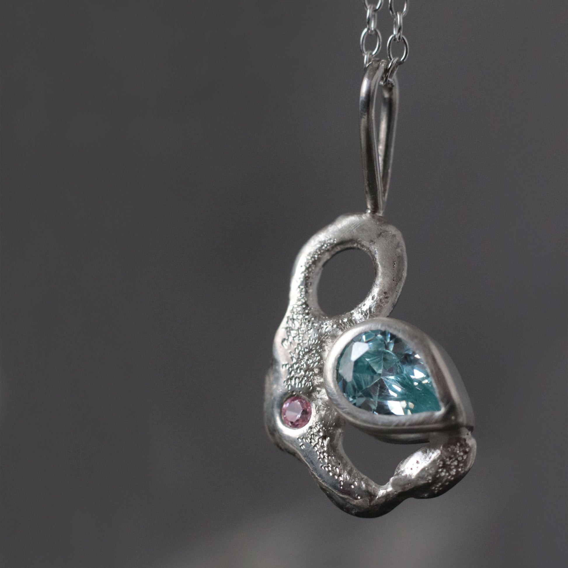 Silver pendant with blue gemstone and pink stone on a dark background
