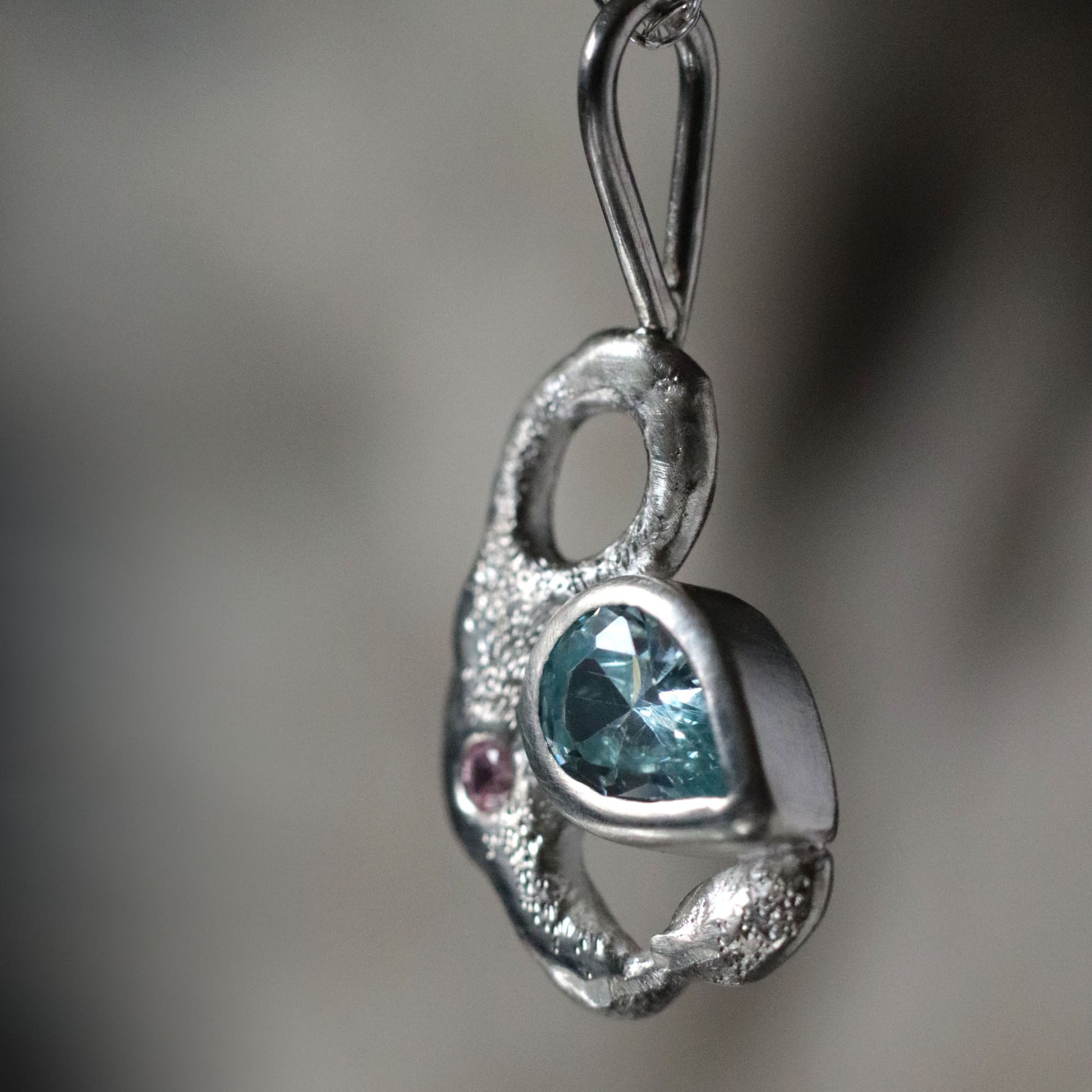 Silver pendant with a blue gemstone on a blurred background