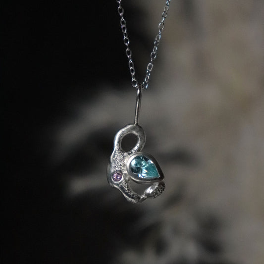 Molten silver pendant with a blue gemstone on a blurred background